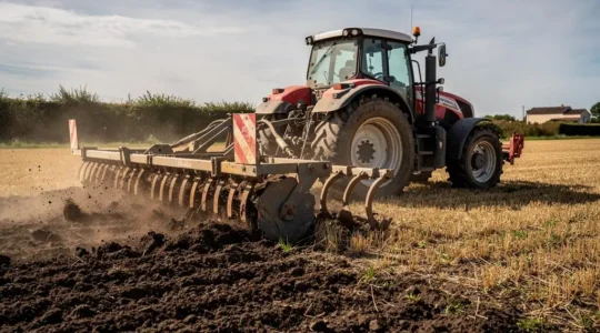Tracteur agricole tirant un décompacteur à dents dans un champ après récolte en France